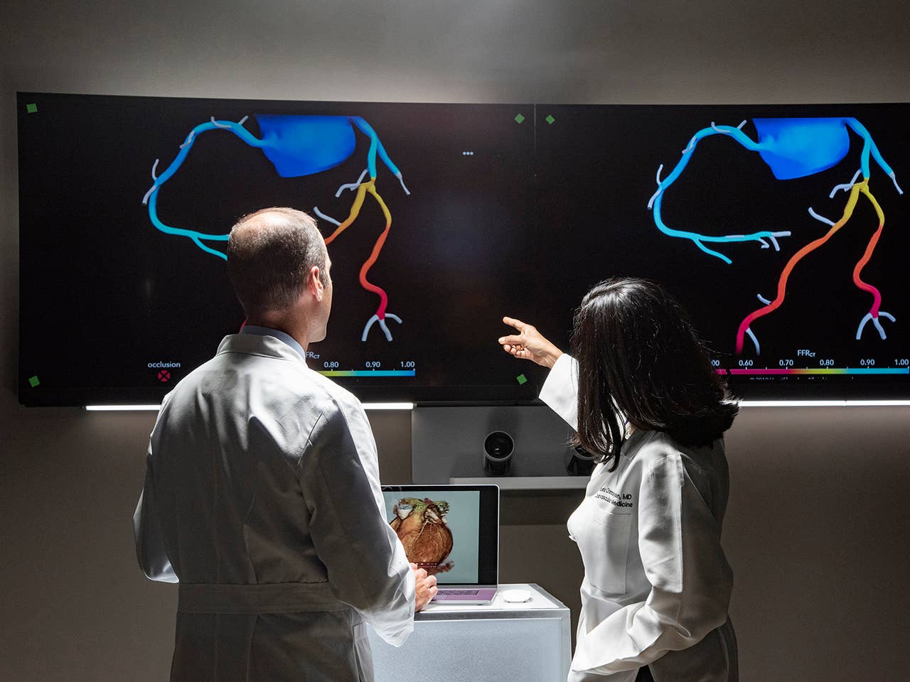 Two doctors examining a computer screen displaying a heart graphic, engaged in a discussion about patient care.