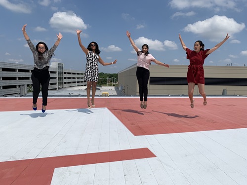 Four women joyfully jumping on a rooftop, showcasing camaraderie and excitement in an urban setting.