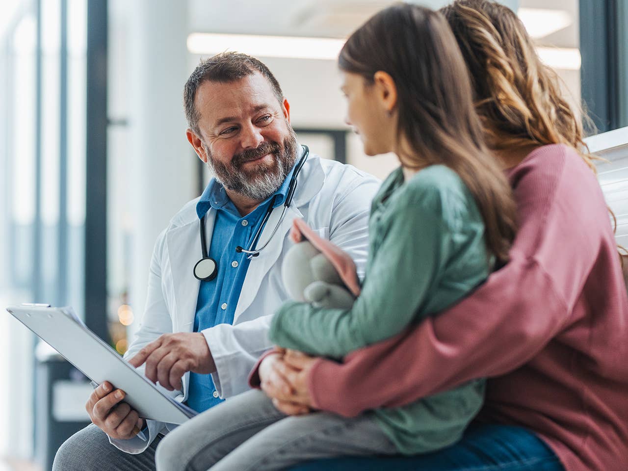 male medical provider speaking to a mother and her child while pointing at a medical chart in his hand