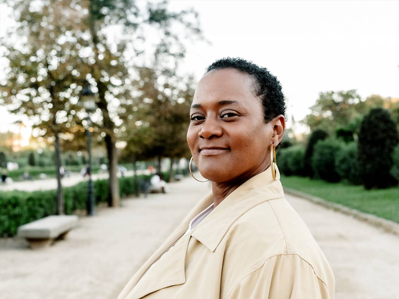 Young Black woman with short hair stands on a path in a park in the evening