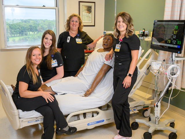 team members posing for picture around a simulation person in a hospital bed