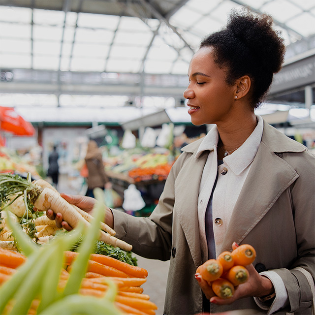 Person selecting fresh carrots and root vegetables at a market, finding healthy foods that fit a budget.