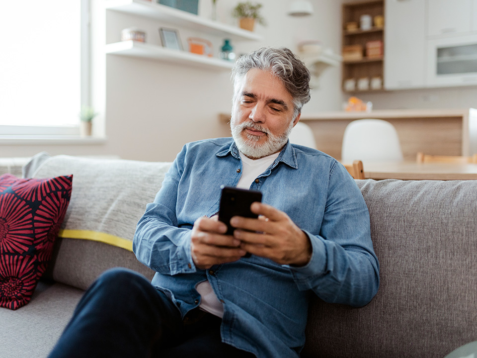 Man sitting on his couch scheduling his next doctors appointment on his cell phone