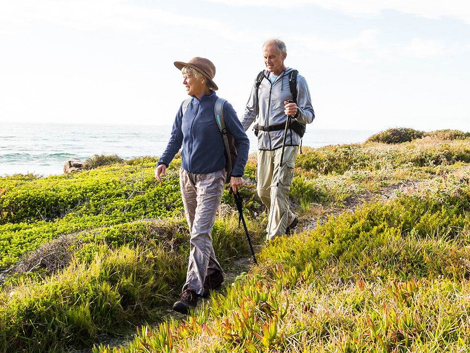 Elderly man and woman hike in wild grasses along a body of water