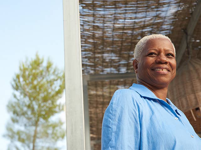Smiling Black woman with short white hair stands in the sunshine outdoors