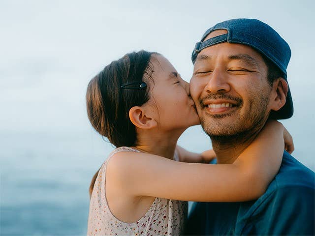 Preteen girl with long brown hair hugging her father and kissing his cheek
