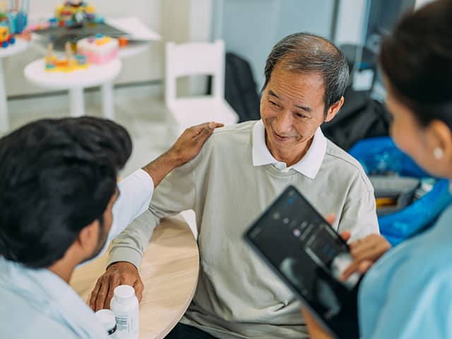 A man speaks with a doctor while a nurse observes the conversation attentively.