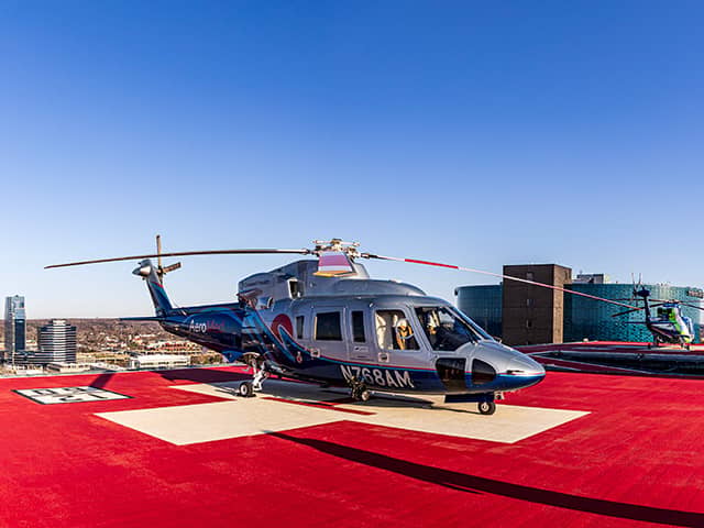 Corewell Health Aero Med helicopter, with silver and blue paint on its body, sitting on a helipad on top of a building