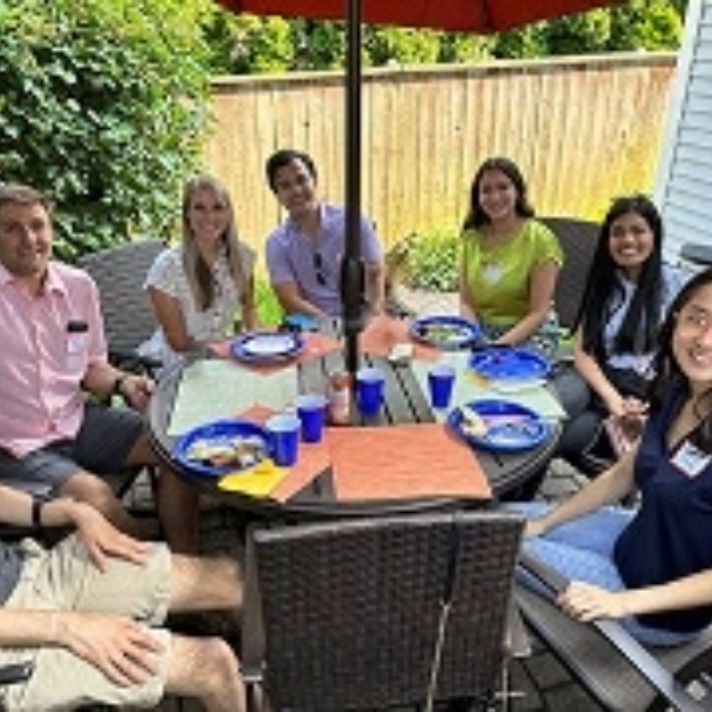 Group of residents sitting around a table with an umbrella eating and drinking during the welcome party event