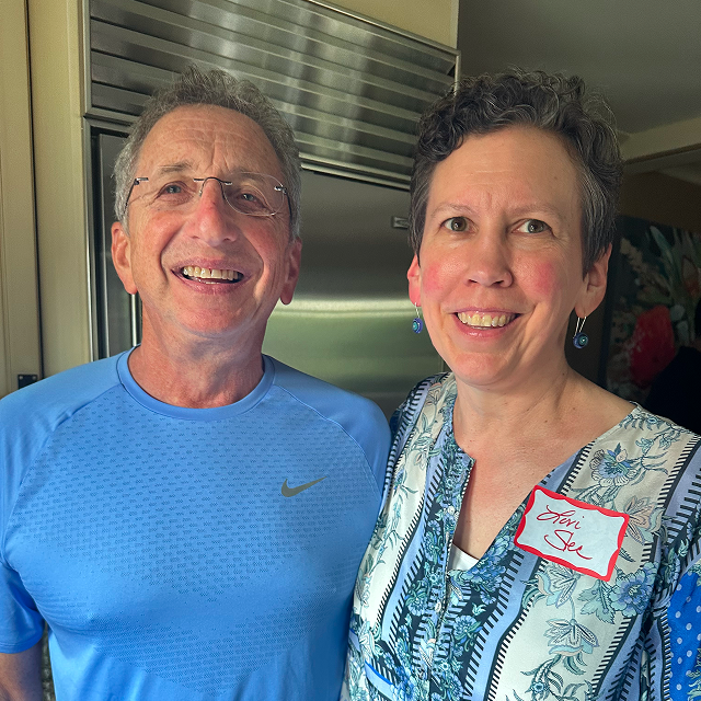 Two attendees pose together indoors, one wearing a blue shirt and the other a patterned top with a name tag.