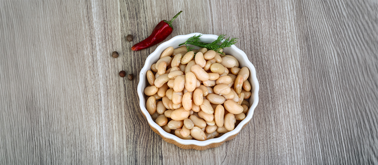 Bowl of white beans with fresh dill and red pepper on a wooden table, highlighting a nutritious ingredient for healthy meals.