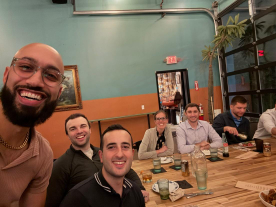 A group of smiling men sitting around a table, posing happily for the camera.