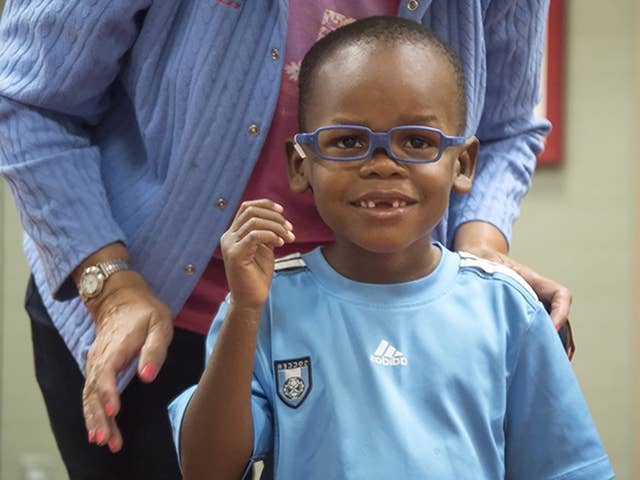 Smiling young Black boy in a light blue shirt wearing blue glasses