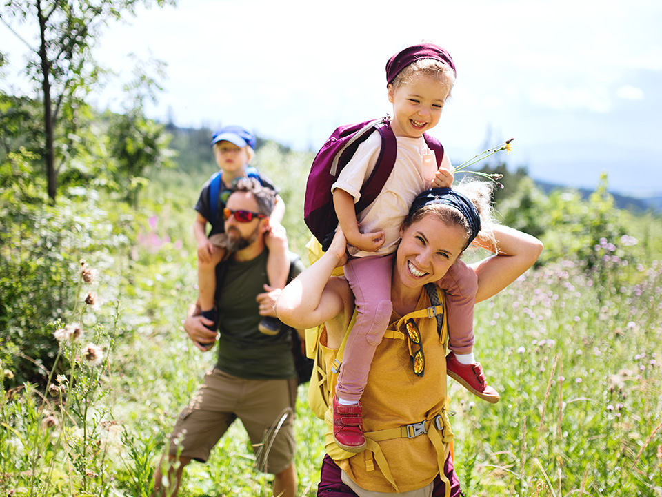 A woman walks with two children through a green field under a clear blue sky.
