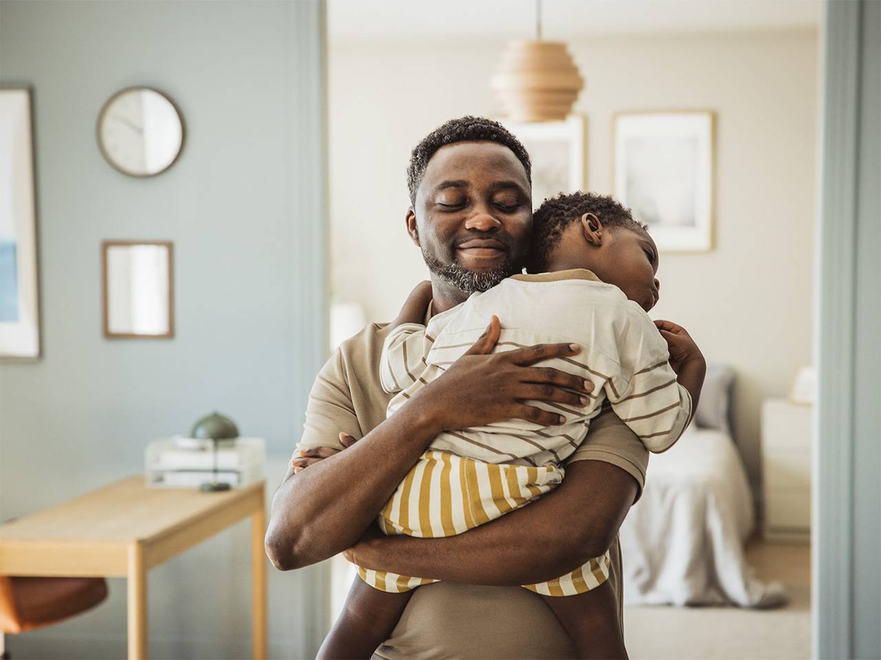 Smiling Black man with dark brown hair and a beard lifts up and hugs his young son