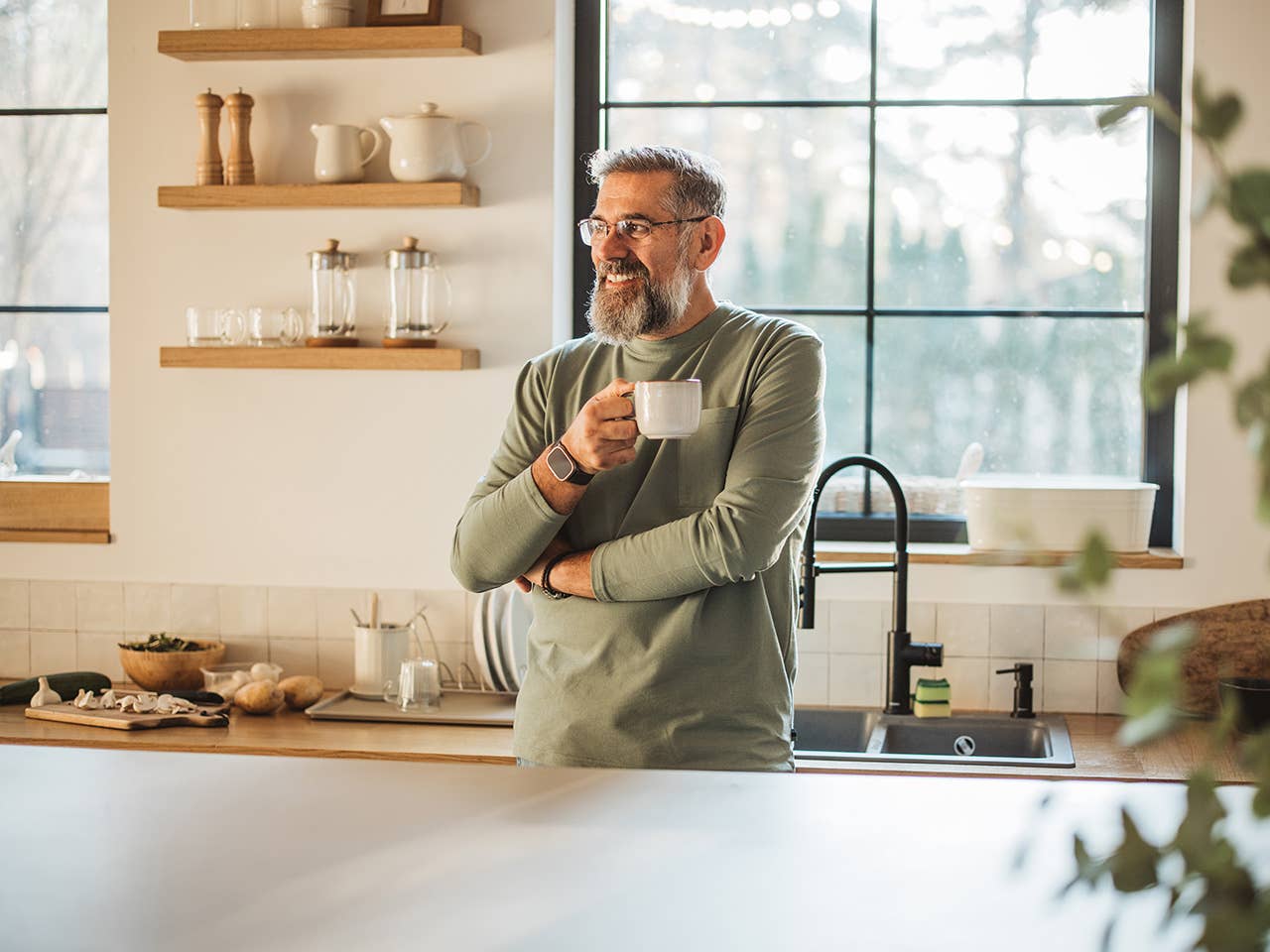Smiling man with grey hair and a grey beard stands in a kitchen holding a coffee mug