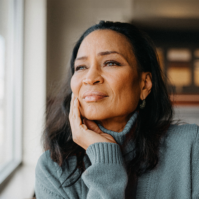 A woman gazes thoughtfully out of a window, her expression reflecting anxiety and depression.