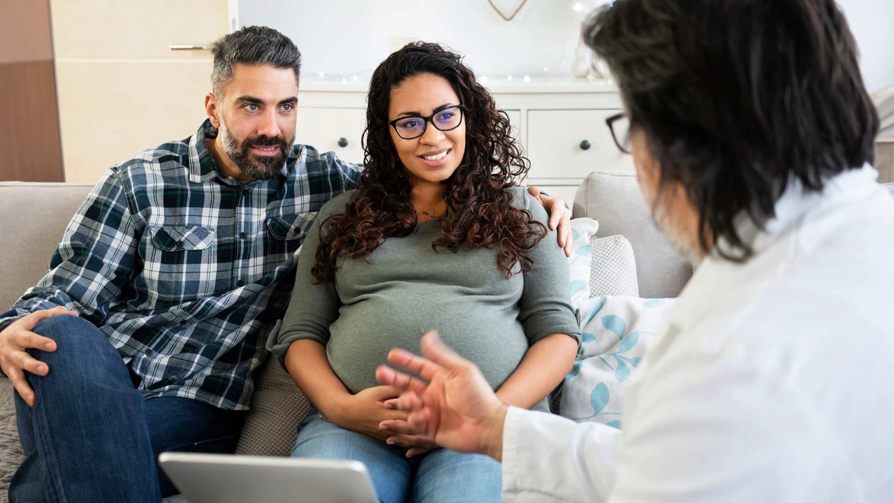 Pregnant woman and her partner sit next to one another while they speak with a Corewell Health women's health specialist