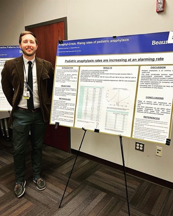 A man stands beside a poster detailing pediatric emergency medicine research projects and topics by various fellows.