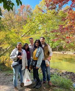 A group of friends poses for a photo by a river, celebrating the vibrant colors of Michigan's fall season at an orchard.