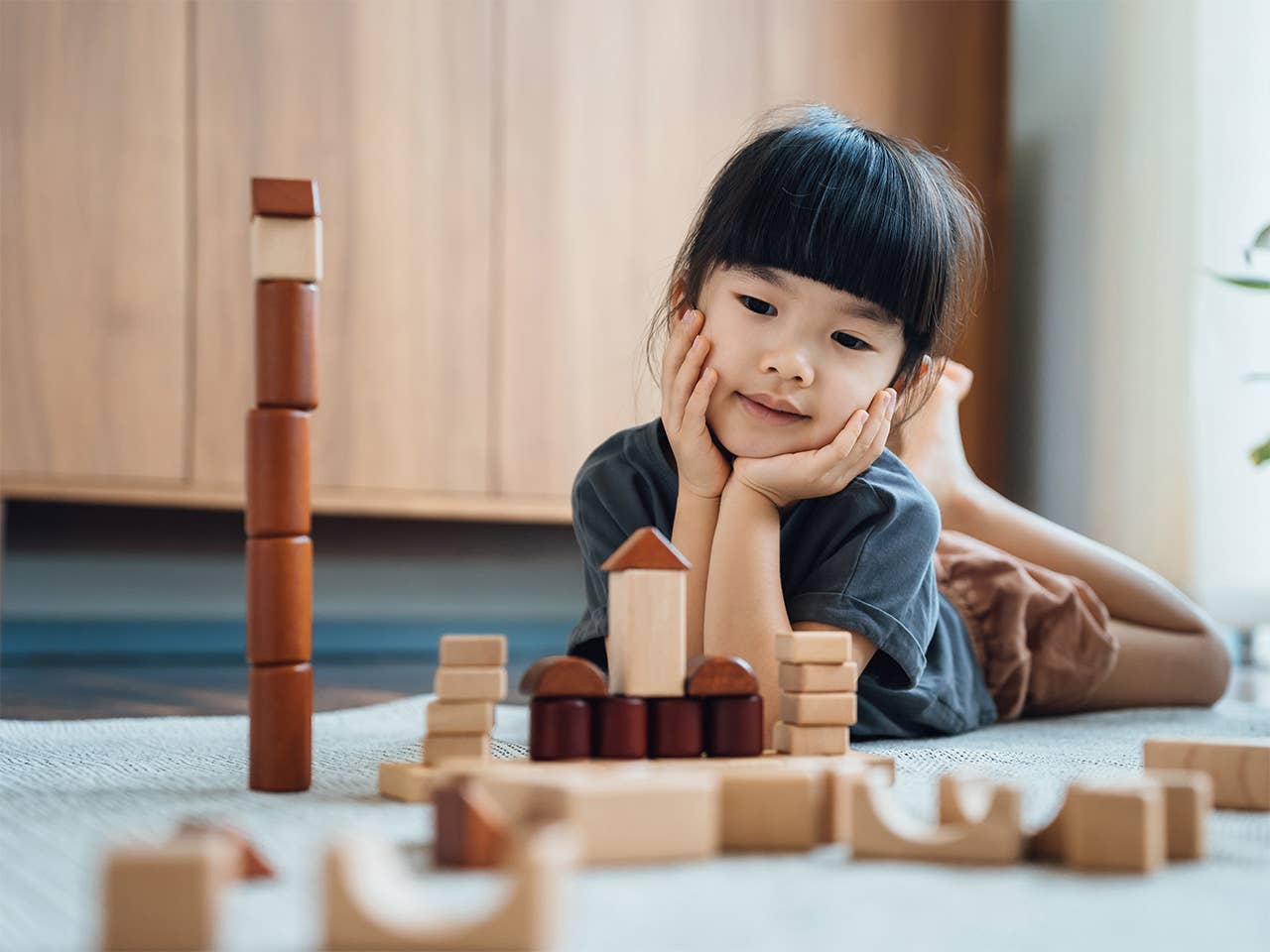 Young Asian girl lays on the floor playing with wooden blocks