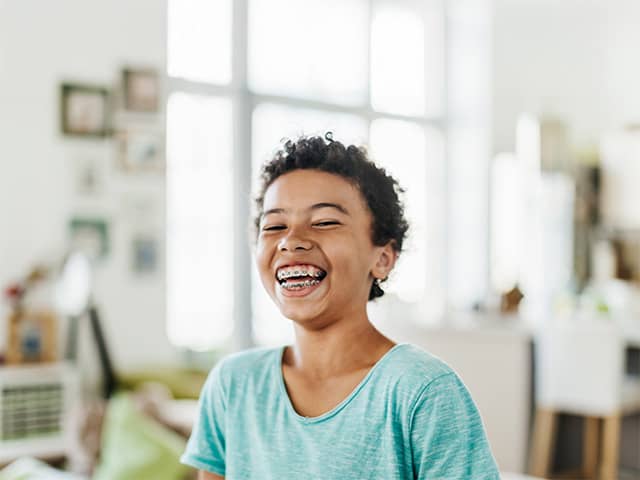 Girl with short curly brown hair and braces on her teeth smiles and laughs inside a sunny room
