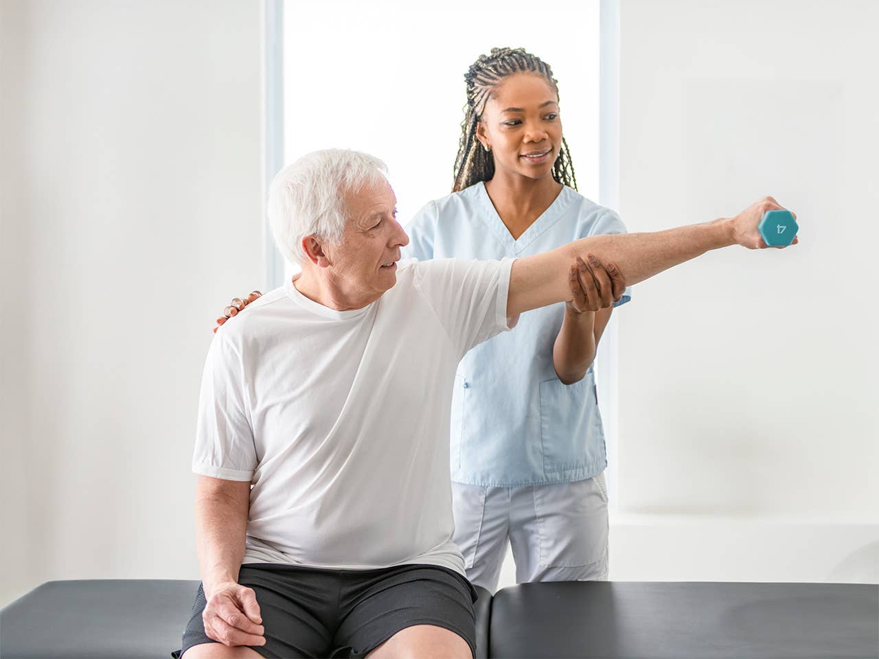 Corewell Health neuro rehab specialist helps an elderly man stretch his arm while holding a weight