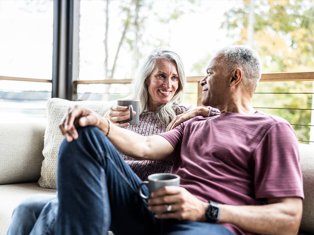 man and woman sitting in chairs outside on a porch drinking coffee