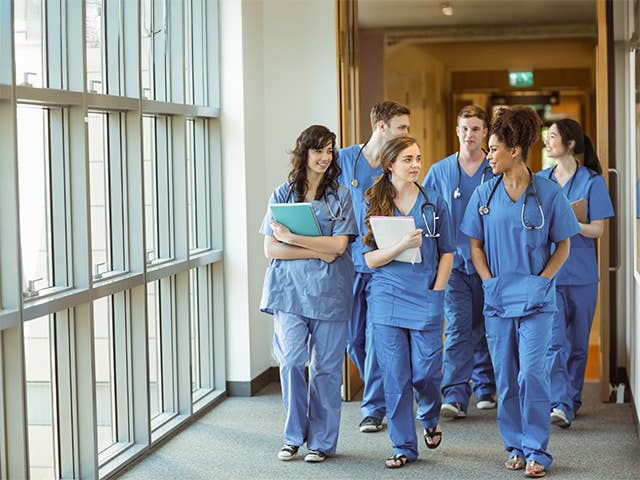 A group of medical students in scrubs walking in a hallway, engaged in conversation.