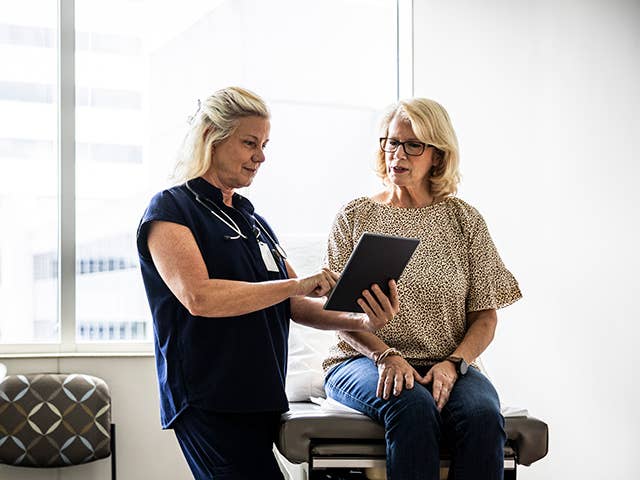 Older white woman sits on an exam table while speaking with a Corewell Health cancer care specialist