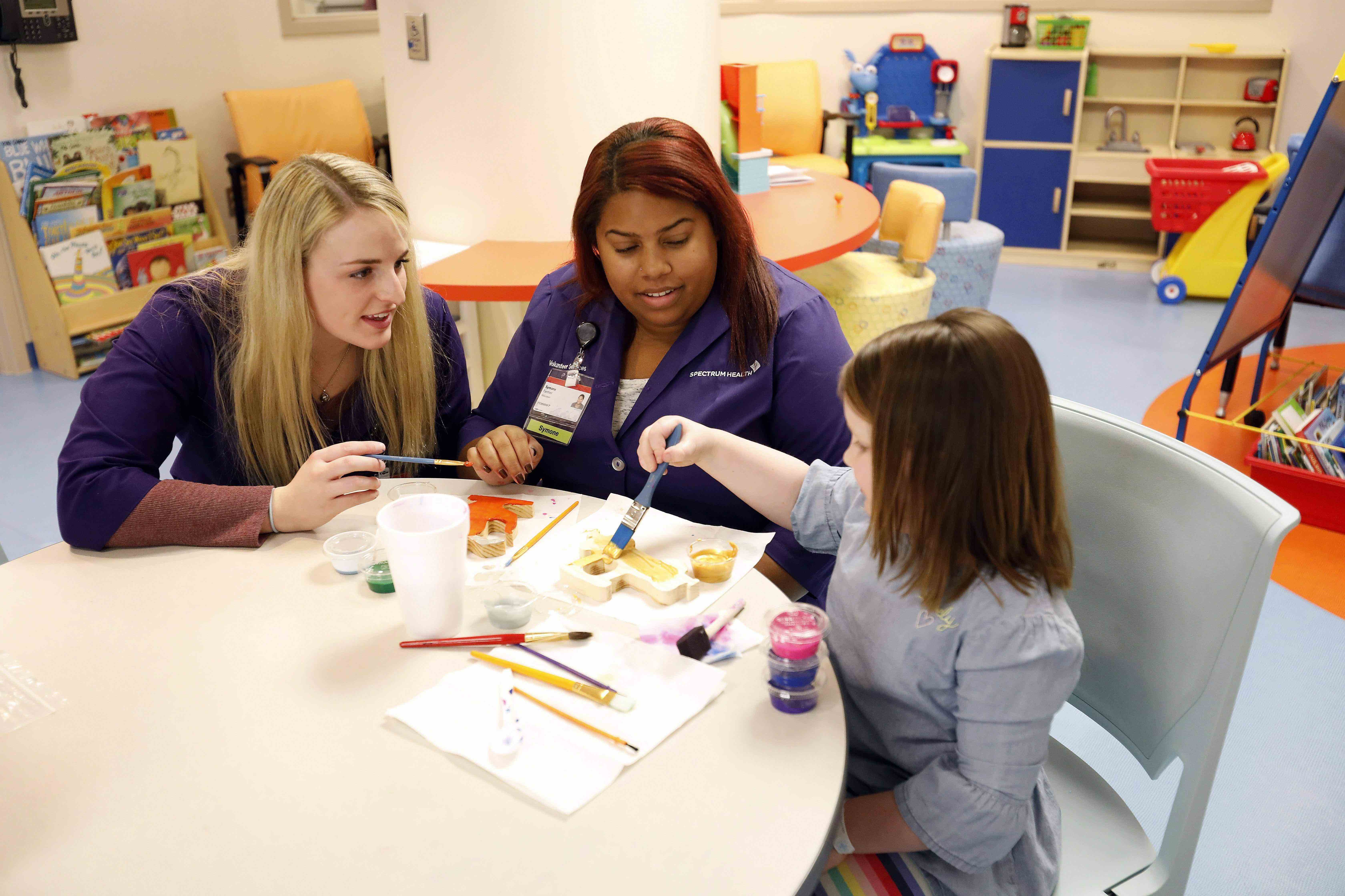 female healthcare worker and mother watching a child work on a craft project