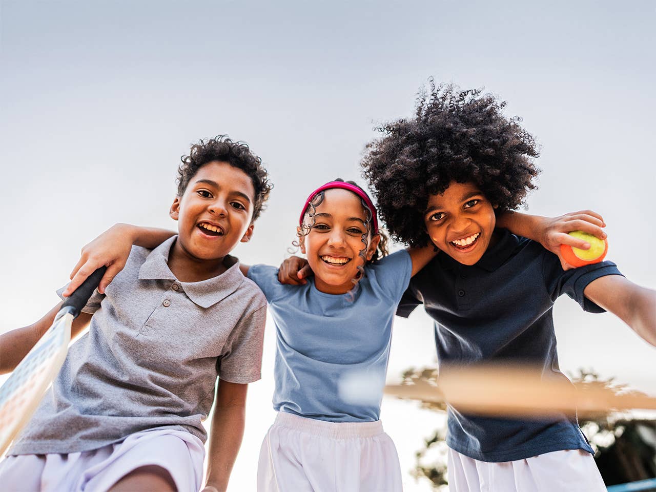 Two young boys and a young girl stand side-by-side with their arms across each other's shoulders, smiling