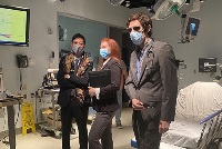 A group of individuals in suits and masks gathered in a hospital room, engaged in simulation activities.