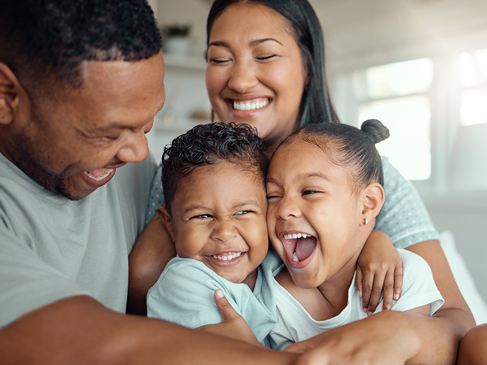 mother and father and two small children hug and smile while at home