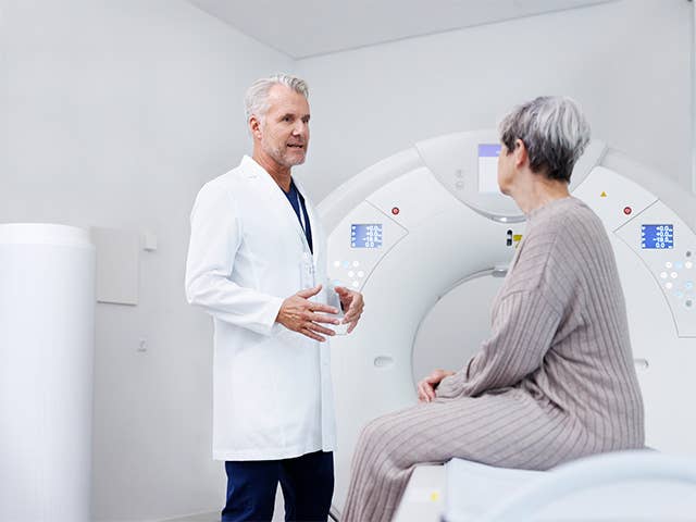 Corewell Health nuclear medicine imaging specialist speaks with a patient as she sits in front of an imaging system