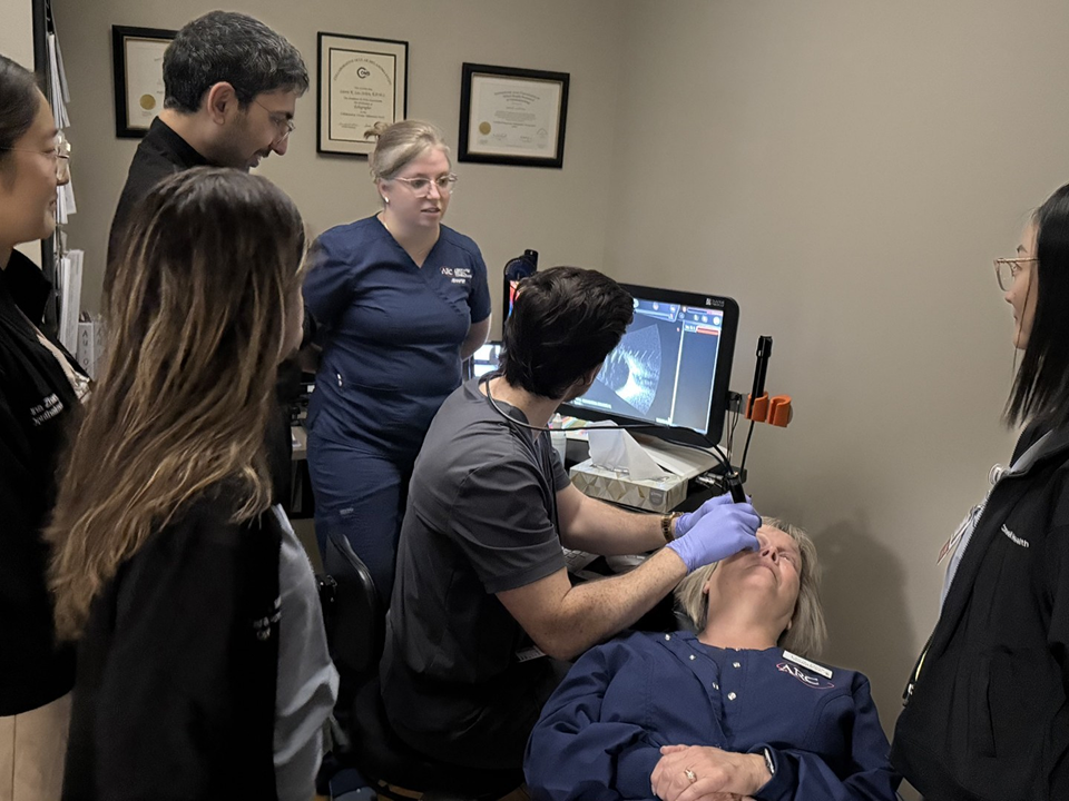 Healthcare staff observe an ultrasound demonstration as a clinician scans a patient and reviews images on a monitor.