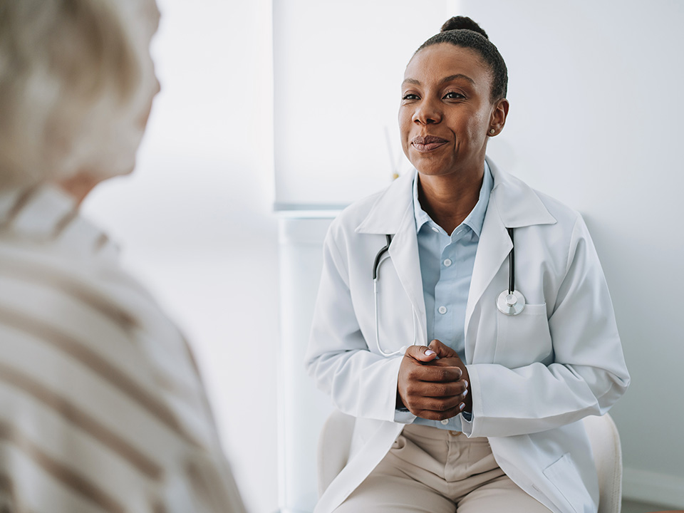 Smiling Corewell Health doctor wearing a lab coat sits across from a patient in an exam room