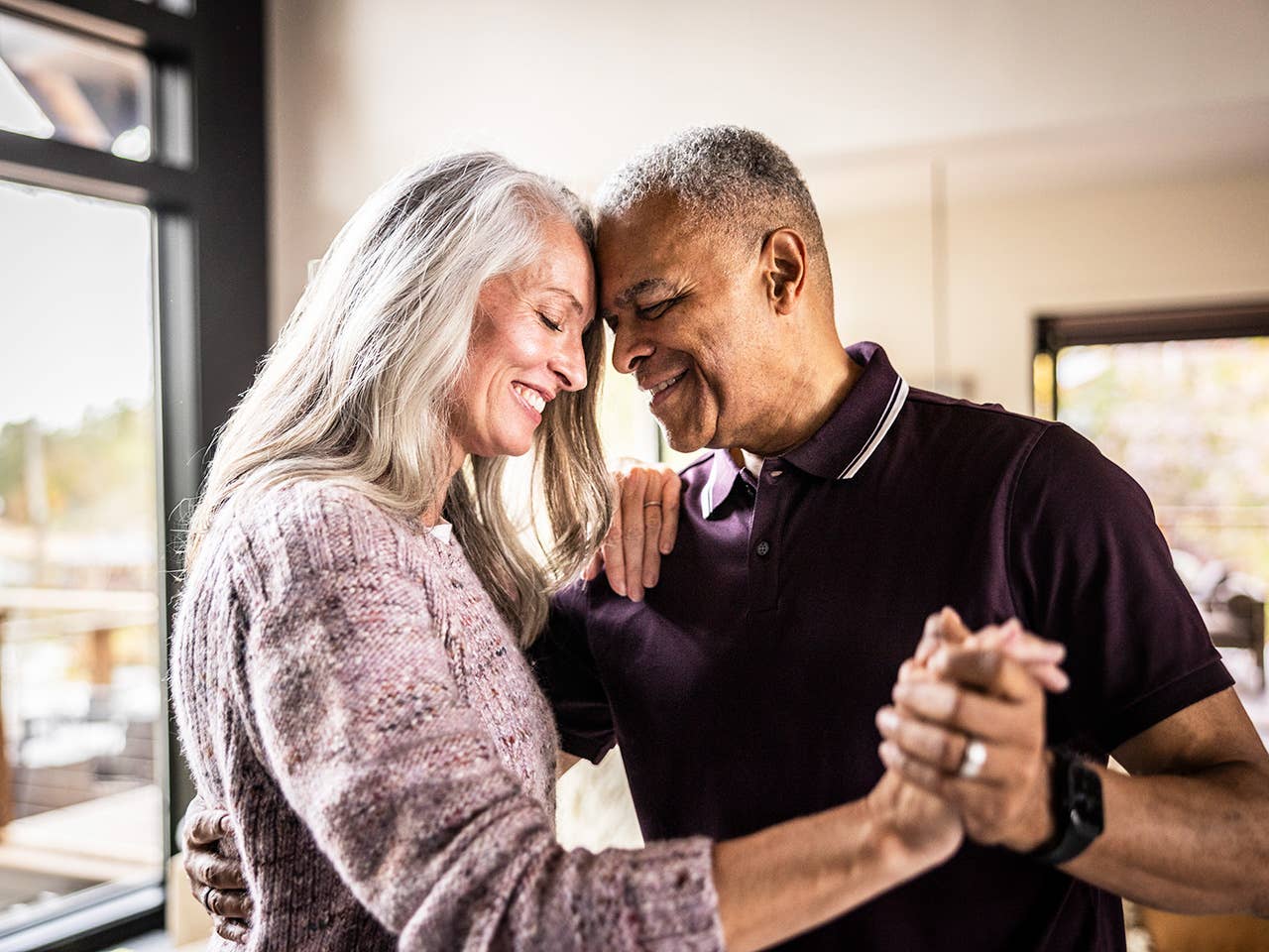 Older man and woman hold hands and smile as they stand face-to-face and dance together