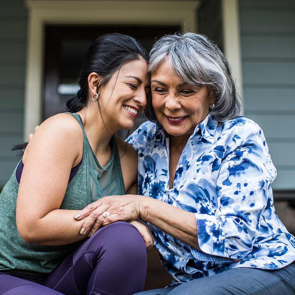 Smiling adult woman sits next to smiling mother hugging her