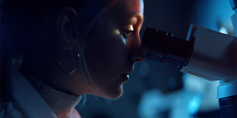 A woman examines a sample through a microscope, showcasing her dedication to research.