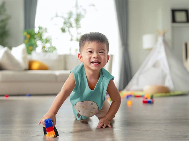 Young Asian boy sits on the floor on his knees while he plays with a plastic block