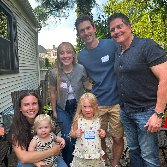 Six attendees, including two young children, pose together outdoors on a backyard patio.