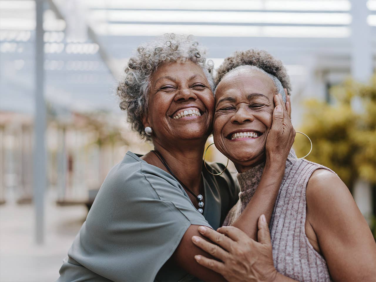 Two smiling older Black women hug each other while standing together