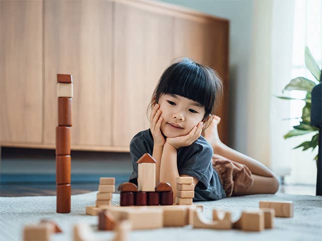 Young Asian girl lays on the floor playing with wooden blocks