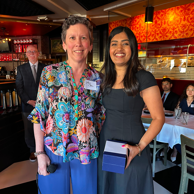 Award recipient posing with a presenter while holding a presentation box at a restaurant recognition event