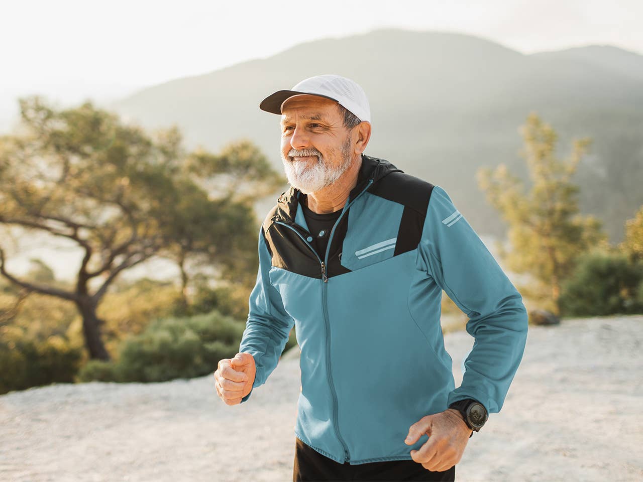 Older man with a grey beard runs outdoors while wearing a light blue jacket