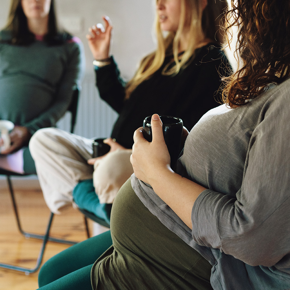 A group of women seated in chairs, with one woman holding a cup, engaged in conversation.