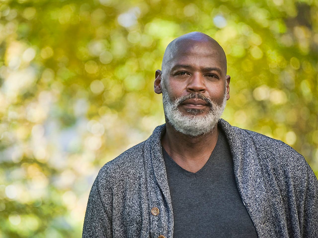 Black man with a grey beard and wearing a black sweater stands outside in the sunshine