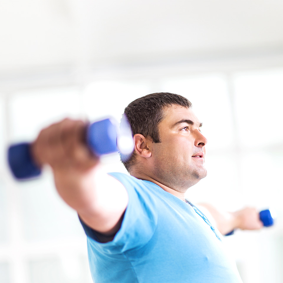 Man in a light blue t-shirt holds hand weights with arms out to his side