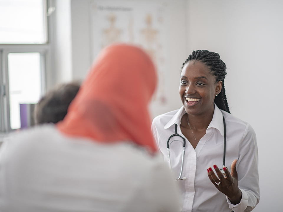 A female doctor converses with a doctor in a medical office setting.